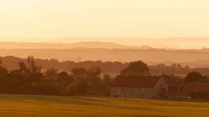 Countrside landscape of rolling hills, old farm houses, all bathed in yellow sunlight (Germany).