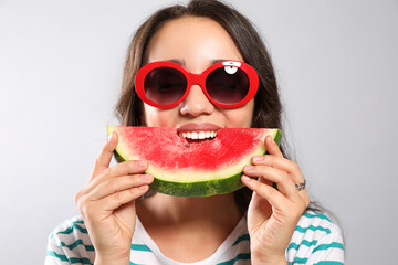 Beautiful young woman eating watermelon on grey background