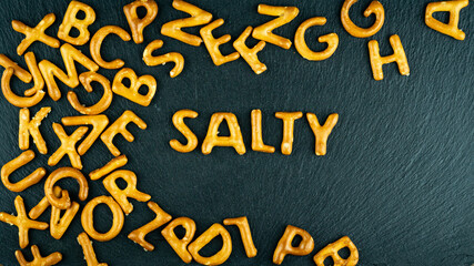 Salty text among bread sticks letters on black background. Salty crisps fonts. Unhealthy diet, junk snacks concept.