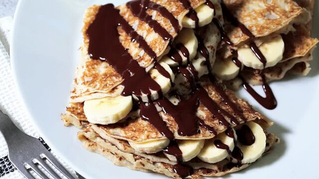 Thin crepes with banana and chocolate on a white plate.