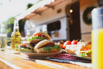 Delicious burgers on wooden table near motorhome. Camping season