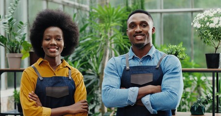 Portrait of happy man and woman in aprons standing at own small flower shop and smiling to camera after reopening African American joyful couple entrepreneurs running own floral business Store concept