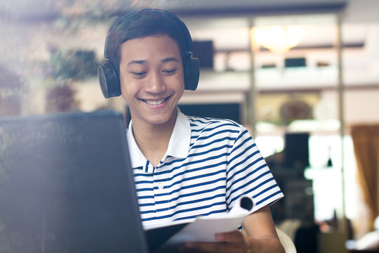 Candit of Asian boy having fun with online teacher by video call on laptop computer at home. smiling young man enjoying online course on application.