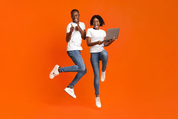 Excited black couple jumping up with laptop
