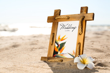Fototapeta premium Beautiful wedding invitation and flower on sandy beach, closeup. Space for text