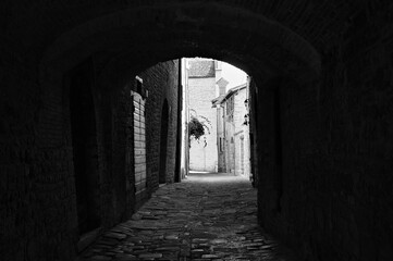 Fototapeta premium The view of an ancient alley under an architectural arch in a medieval Italian village (Gubbio, Umbria, Italy)