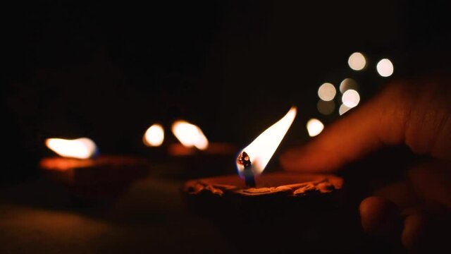 Hand putting oil lamp, diya on the house wall during diwali festival with blurred bokeh lights in background