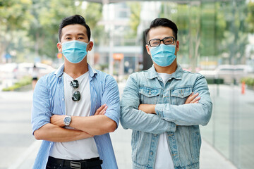 Serious confident young Asian men standing outdoors with arms folded and looking at camera