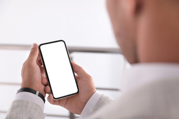 Man holding mobile phone with empty screen indoors, closeup