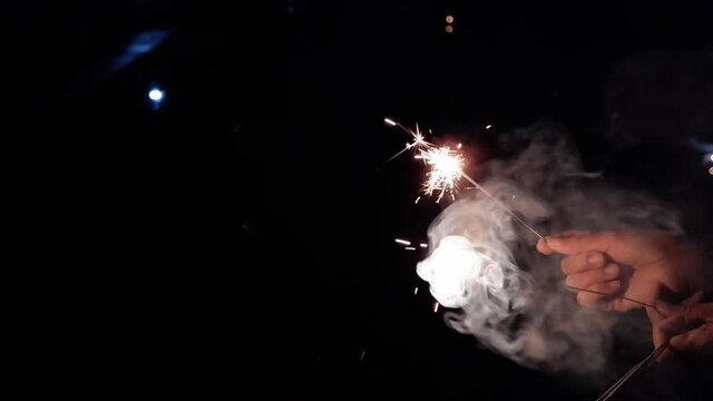 Slow video clip of a yellow scab splashing from fireworks in hand  and white smoke floating on a black background.