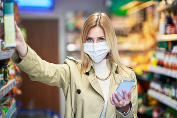 Adult woman in medical mask using smartphone and shopping for groceries