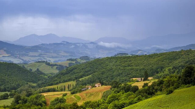 Wind blowing rain storm clouds timelapse over fields and hills in Italy, summer nature outdoor landscape panorama view. Green and yellow grass, natural scenery. High quality 4k footage