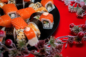 Different kind of rolls and sushi on black plate and Christmas decoration isolated over red background