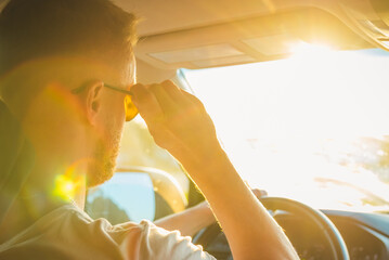 A man sits behind the wheel of his car on a sunny day