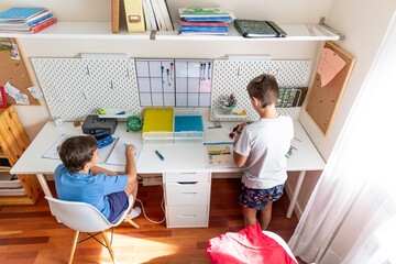 Two boys doing homework in their bedroom one sitting and the other one standing.