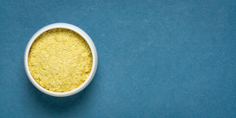 nutritional organic yeast flakes in a small ceramic bowl against handmade textured paper with a copy space, nutrition supplement, baking and cooking
