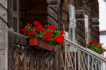Fototapeta na wymiar The facade of the authentic wooden house is decorated with carved columns and railings. Old wooden house facade. Blooming red geraniums on the railing of an old wooden house.