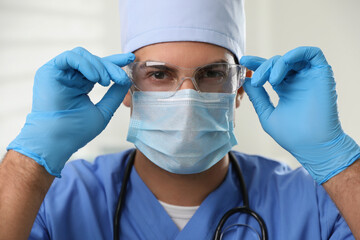 Doctor in protective mask, glasses and medical gloves against light background