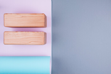 Top view of blue pink yoga mat and two wooden blocks on pastel grey background. Yoga, pilates or sport concept. Copy space.