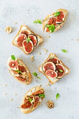 Crispy bruschetta with soft ricotta, ripe figs, walnuts and pine nuts, mint and honey on a light background. Figs fruit toast on marble table with honey and walnut. Top View.