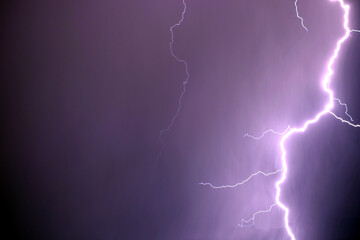 Many bright lightning discharges in the purple stormy sky under heavy purple rain clouds