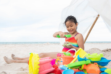 Fototapeta premium cute little girl playing on the beach on summer holidays. Happy child playing with sand at the beach. kid wear brightly colored swimwear and colorful toys.
