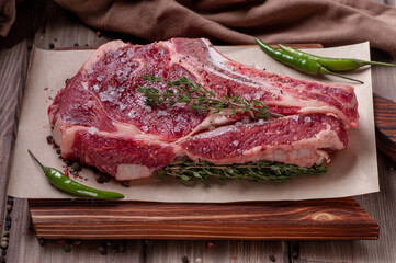 Raw uncooked beef steak. A large piece of meat on the bone lies on a wooden board with spices and fresh herbs.