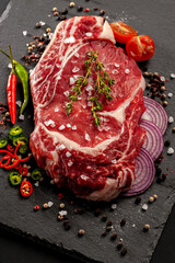 Raw uncooked beef steak. A large piece of meat on the bone lies on a wooden board with spices and fresh herbs.