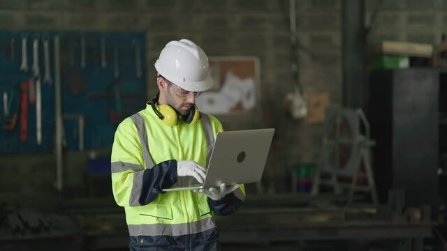 Mechanical Engineer in Hard Hat Wearing Safety Jacket Uses Laptop working in the Manufacturing Factory
