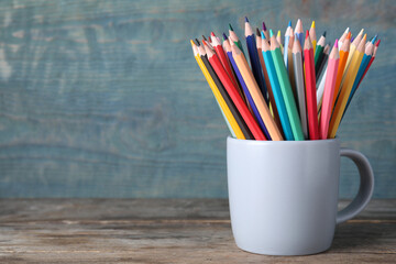 Obraz premium Colorful pencils in cup on wooden table. Space for text