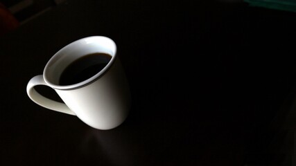Angled white mug with black coffee on black background