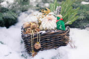 A basket with Christmas children's toys and Christmas tree decorations stands in the snow next to the spruce