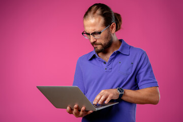 Man in glasses standing with laptop against pink background