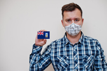 Man in checkered shirt show Falkland Islands flag card in hand, wear protect mask isolated on white...