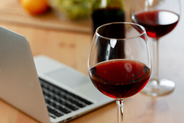 Laptop and glass of red wine on wooden kitchen table