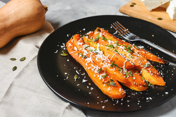 Baked slices of pumpkin with seasonings and feta on concrete background.