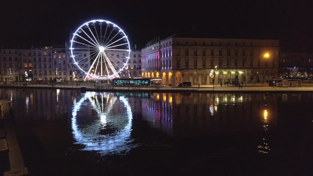Static shot of the ferris wheel and the town hall at night, with their reflection on the Nive river, Bayonne, France.