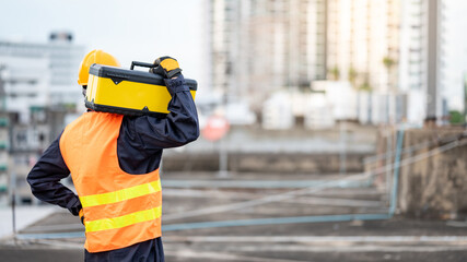 Asian maintenance worker man wearing protective suit and safety helmet carrying work tool box at construction site. Equipment for civil engineering project