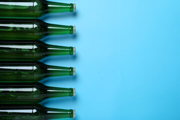 Bottles of beer on light blue background, flat lay. Space for text