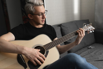 Man with white hair wearing glasses on the couch playing guitar at home