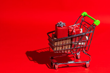 Supermarket trolley full of Christmas gifts on a red background in pop-art style with hard shadow. Gifts theme for new year, christmas, black friday.