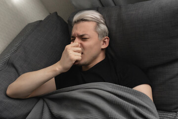 Man with white hair is sick while lying on the sofa at home