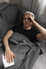 Man with white hair is sick while lying on the sofa at home