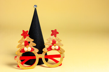 Black Christmas tree with masquerade glasses on a yellow background. Christmas in high-tech, modern style.