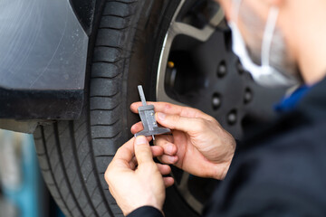 Mechanic checking checking the depth of car tire tread.  Car maintenance and auto service garage concept.