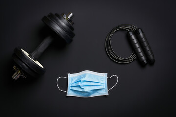 fitness gear dumbbell, jumping rope and protective mask on dark surface