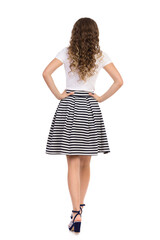 Woman In Striped Skirt And High Heels Is Walking With Hands On Hip. Rear View.