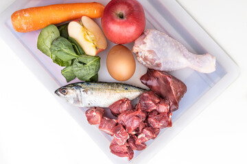 Overhead view of ingredients of barf raw food recipe for dogs consisting meat, organs, fish, eggs and vegetable on chopping board