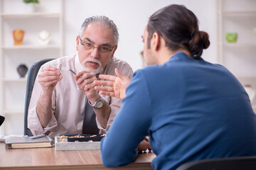 Young man visiting old male jeweler
