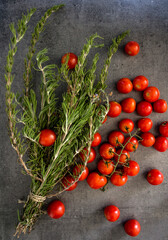 Fototapeta na wymiar Rosemary bounds and cherry tomatoes on dark grey textured background. Top view photo of fresh vegetables and herbs. 